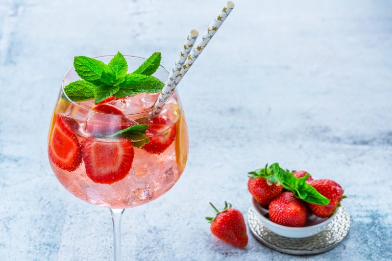 Strawberry Gin Smash Cocktail with two straws topped with fresh mint and served with a bowl of strawberries